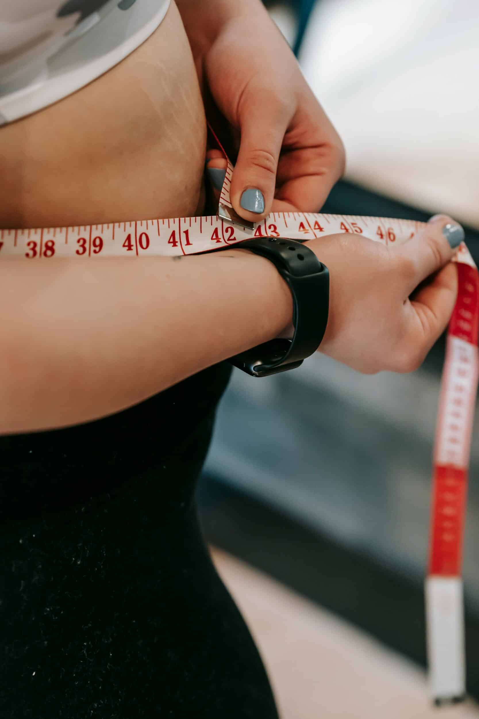 A person measuring their waist with a measuring tape.